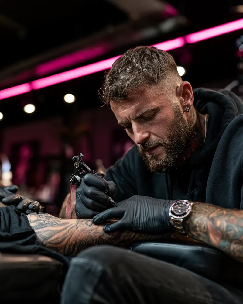 Tattoo artist working on a client's forearm in a studio